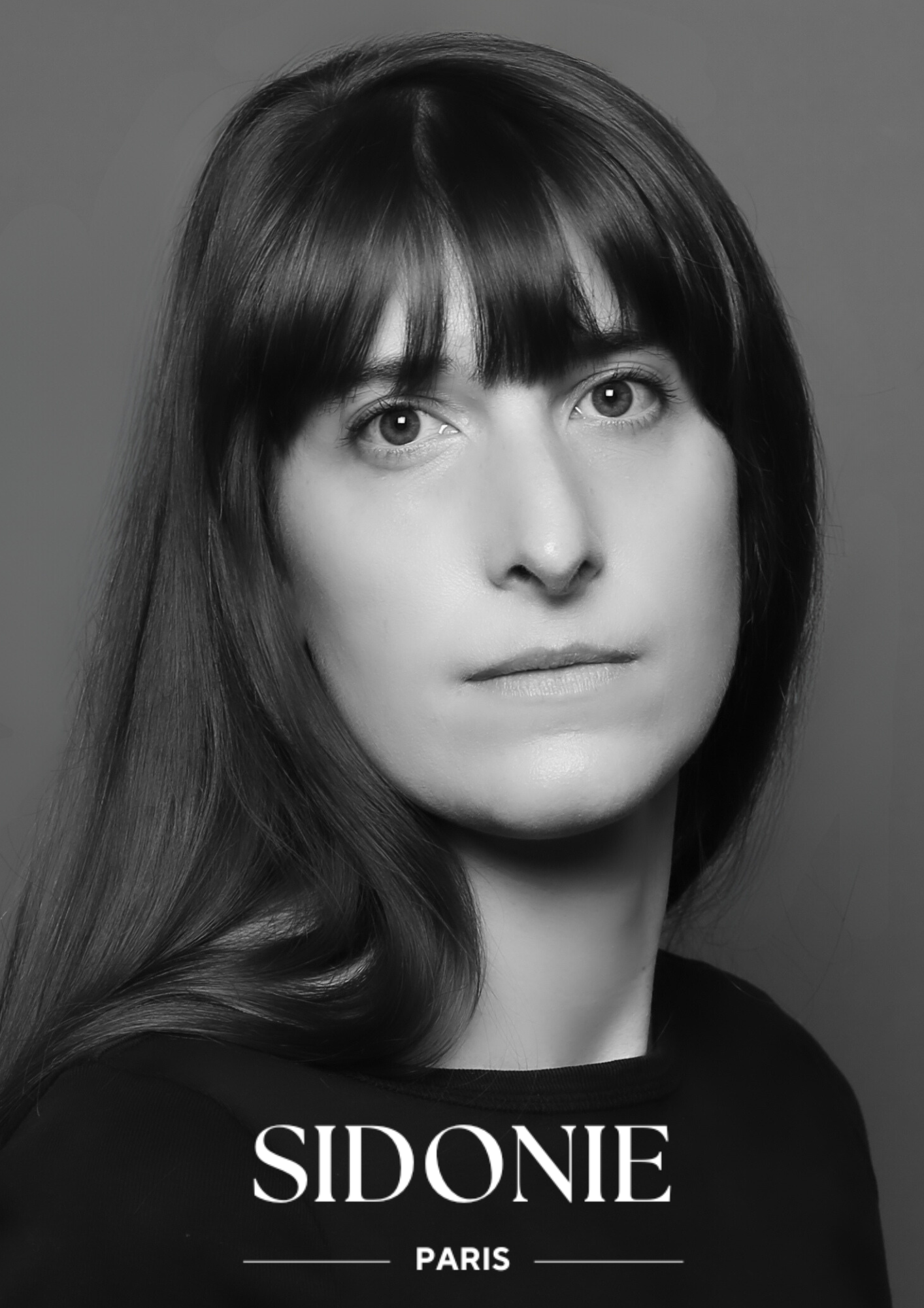 Portrait en noir et blanc d'Elisa Girardet avec les cheveux détachés, regardant directement vers l'objectif, sur un fond uni. Le texte SIDONIE PARIS est au bas de l'image, capturant l'essence d'une mode créatrice visionnaire.