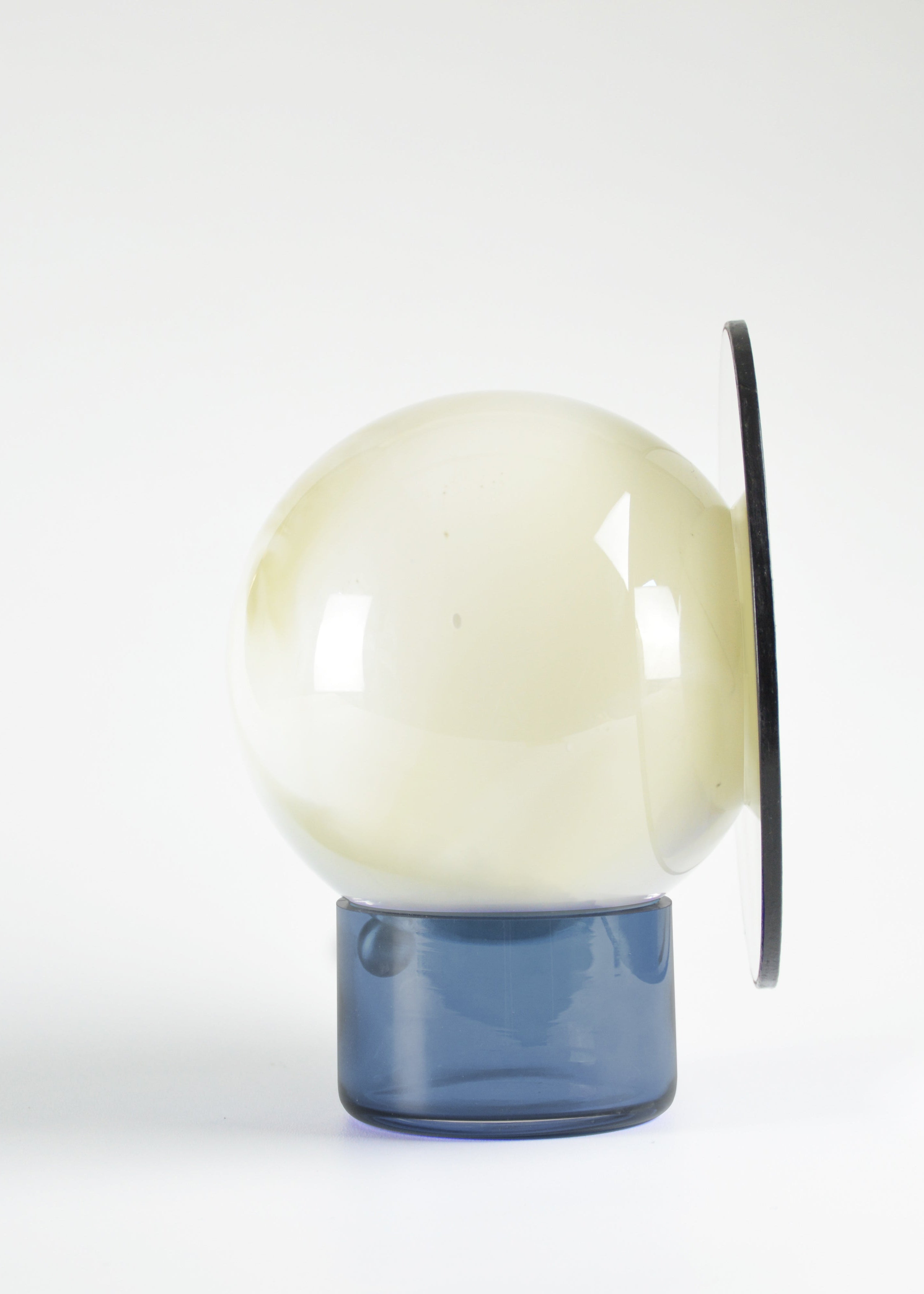 Miroir orientable cerclé de cuir, composé d’une sphère en verre soufflé au décor blanc marbré et d’une base en verre bleu, vu de profil.