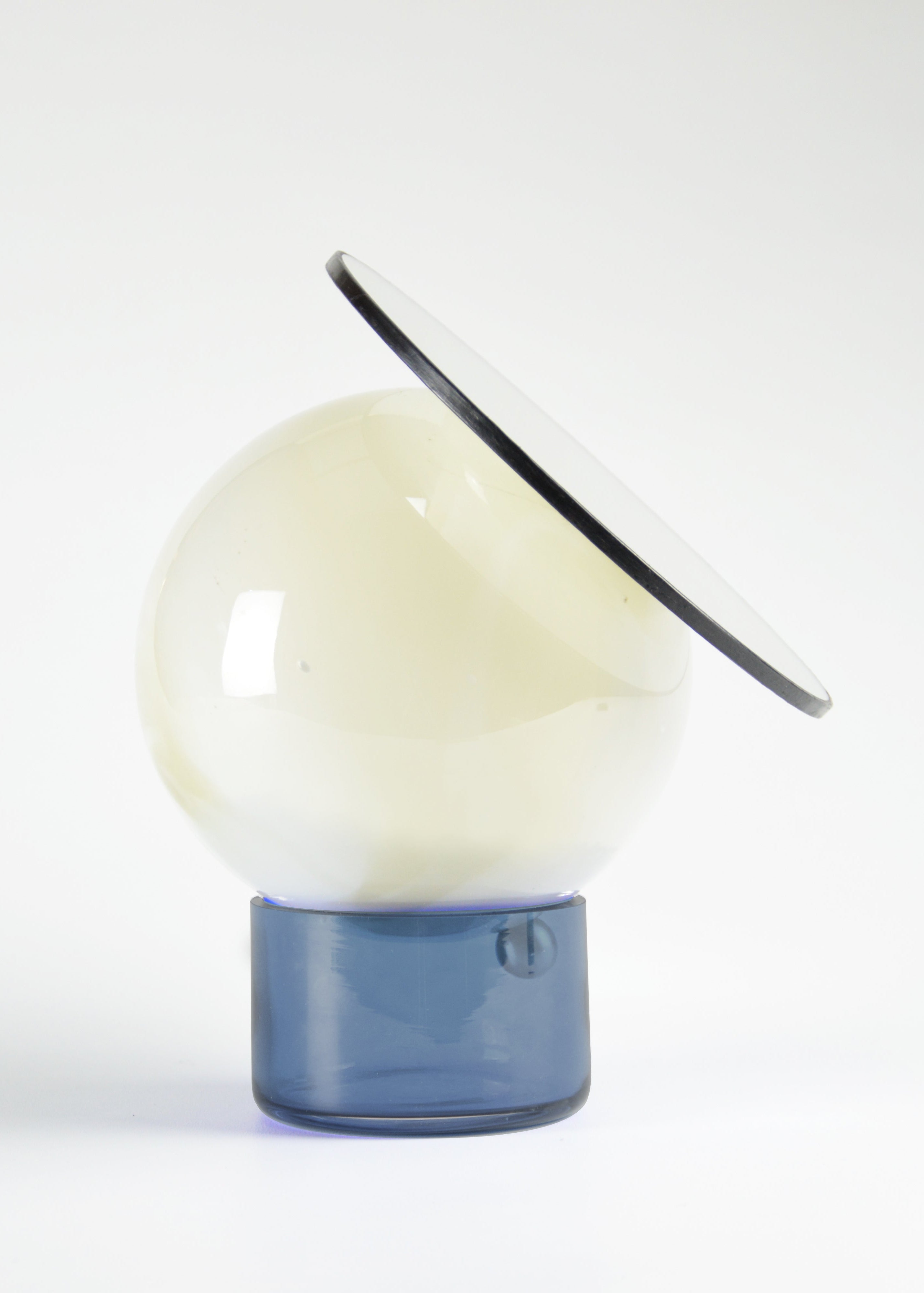 Miroir orientable cerclé de cuir, composé d’une sphère en verre soufflé au décor blanc marbré et d’une base en verre bleu avec le miroir incliné vers le haut.