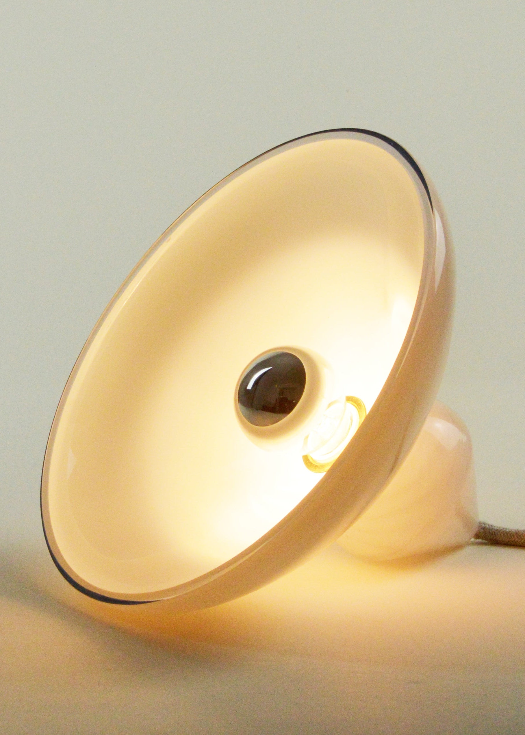 Lampe à poser allumée, fabriquée em Francecomposée d’une base de verre soufflé à décor de marbrures et d’un réflecteur de verre blanc en forme d’ellipse.