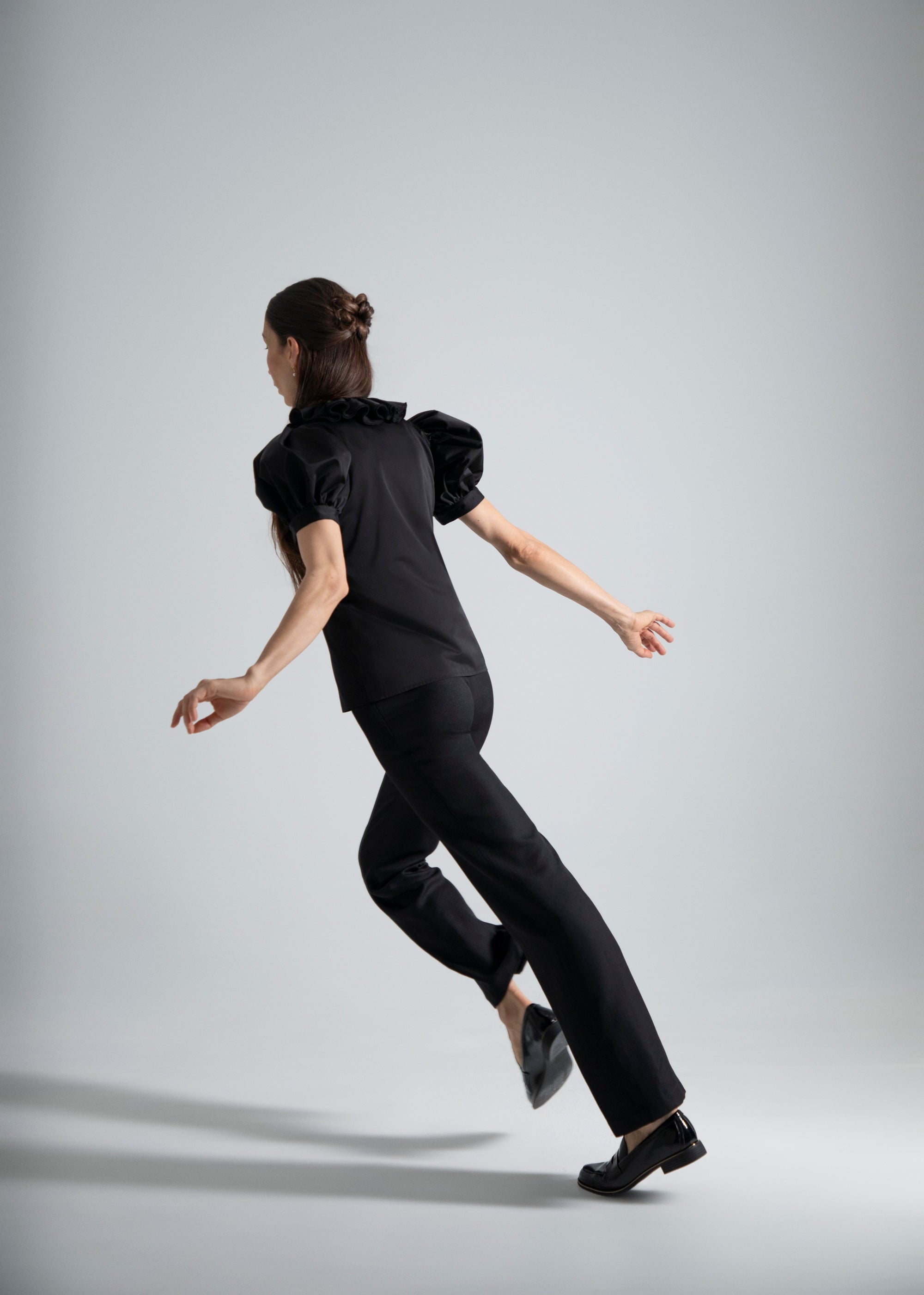 Femme en habillée en Sidonie Paris portant le top noir Vesper et le Pantalon Salomé, courant avec son ombre.