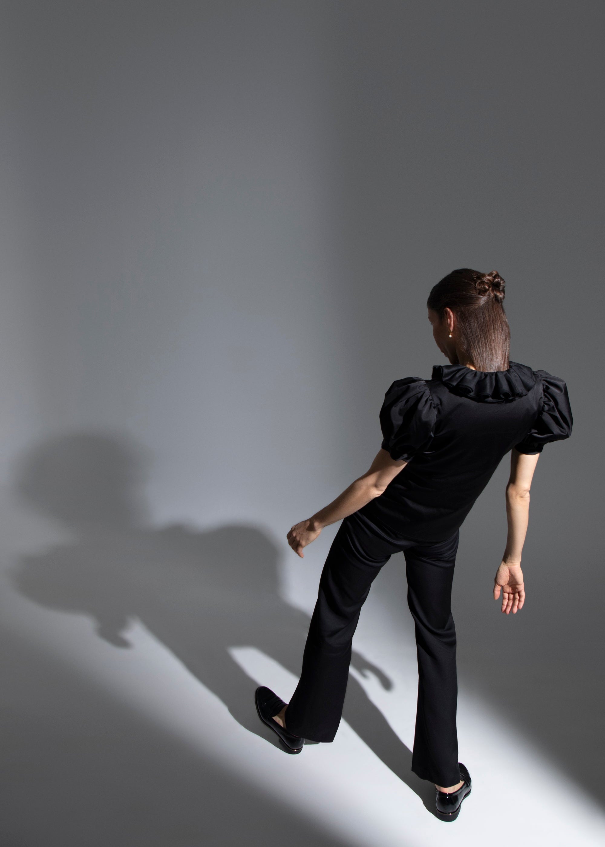 Photo artistique d'une femme portant le top noir Vesper et le pantalon Salomé, que l'on voit de dos regardant son ombre.