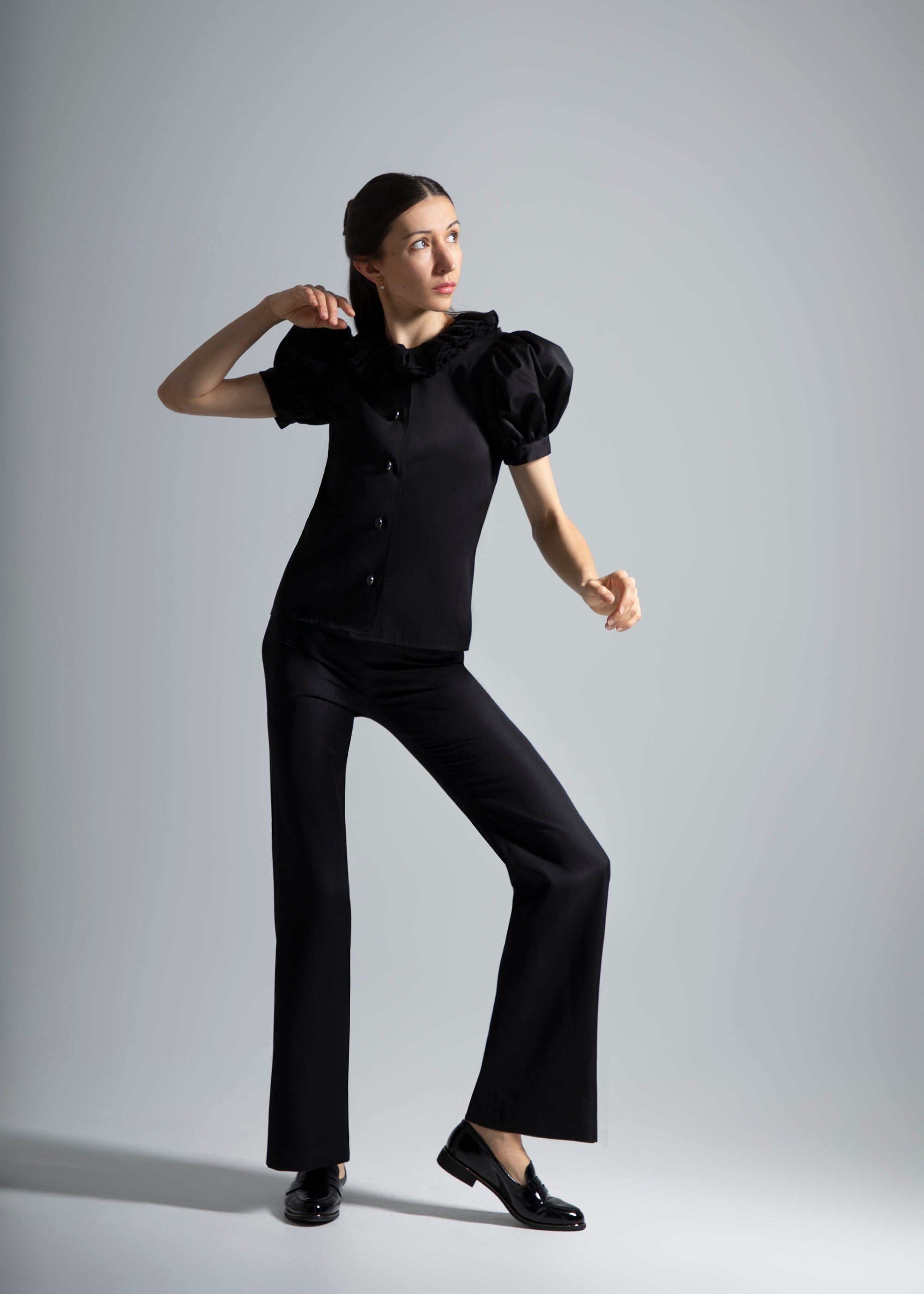 Une femme habillée en vêtements noirs Sidonie Paris pose de plain pied avec le top noir Vesper et le pantalon Salomé, jouant avec l'ombre et la lumière.