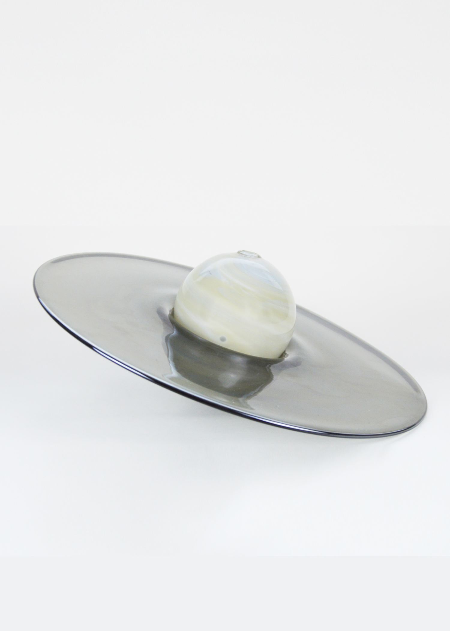 Soliflore, fabriqué en France, composé d’une sphère ivoire aux décors de marbrures posée dans un réceptacle en verre noir, vu de profil.