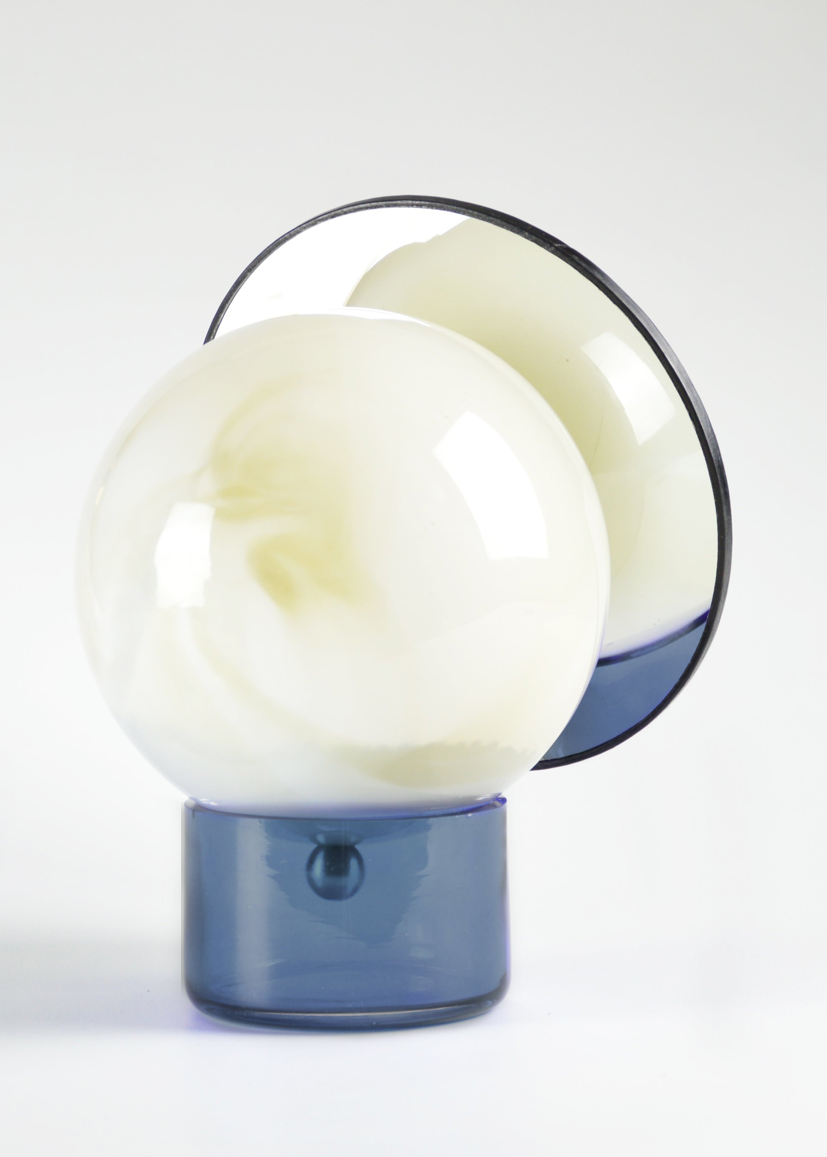 Miroir orientable cerclé de cuir, composé d’une sphère en verre soufflé au décor blanc marbré et d’une base en verre bleu, vu de dos.