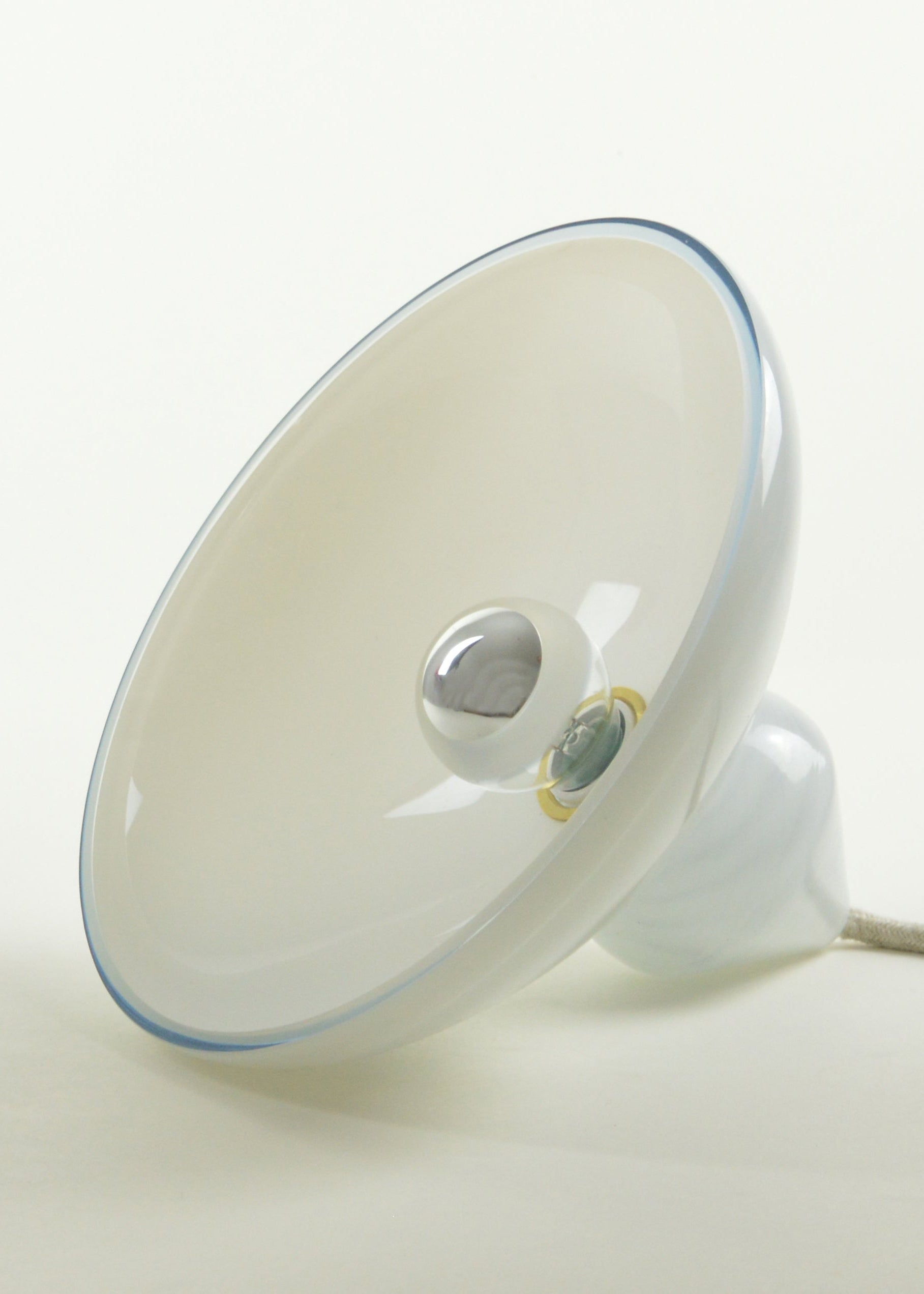 Lampe à poser, fabriquée en France, vu de profil. Elle est composée d’une base de verre soufflé à décor de marbrures et d’un réflecteur de verre blanc en forme d’ellipse.