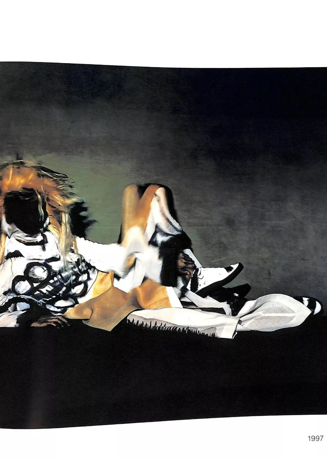 Mannequin allongé portant des vêtements blancs avec des motifs noirs, ainsi qu'une touche de beige du designer Miyake, photographié par Irving Penn.
